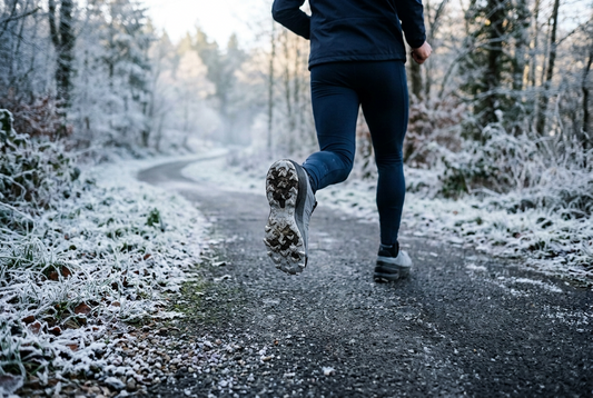 Runner wearing winter running shoes on a cold paved path with light frost along the edges